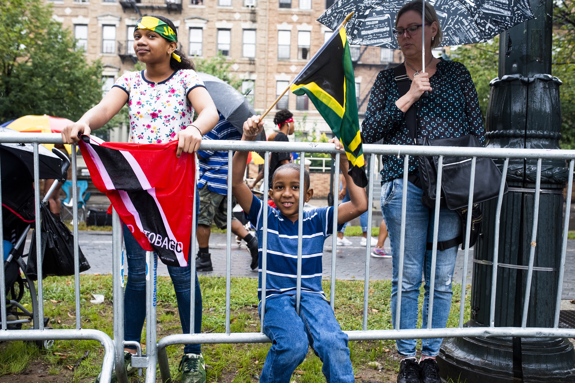 A girl holds the flag for Trinidad and Tobago on the left while a boy proudly waves the Jamaican flag next to her.