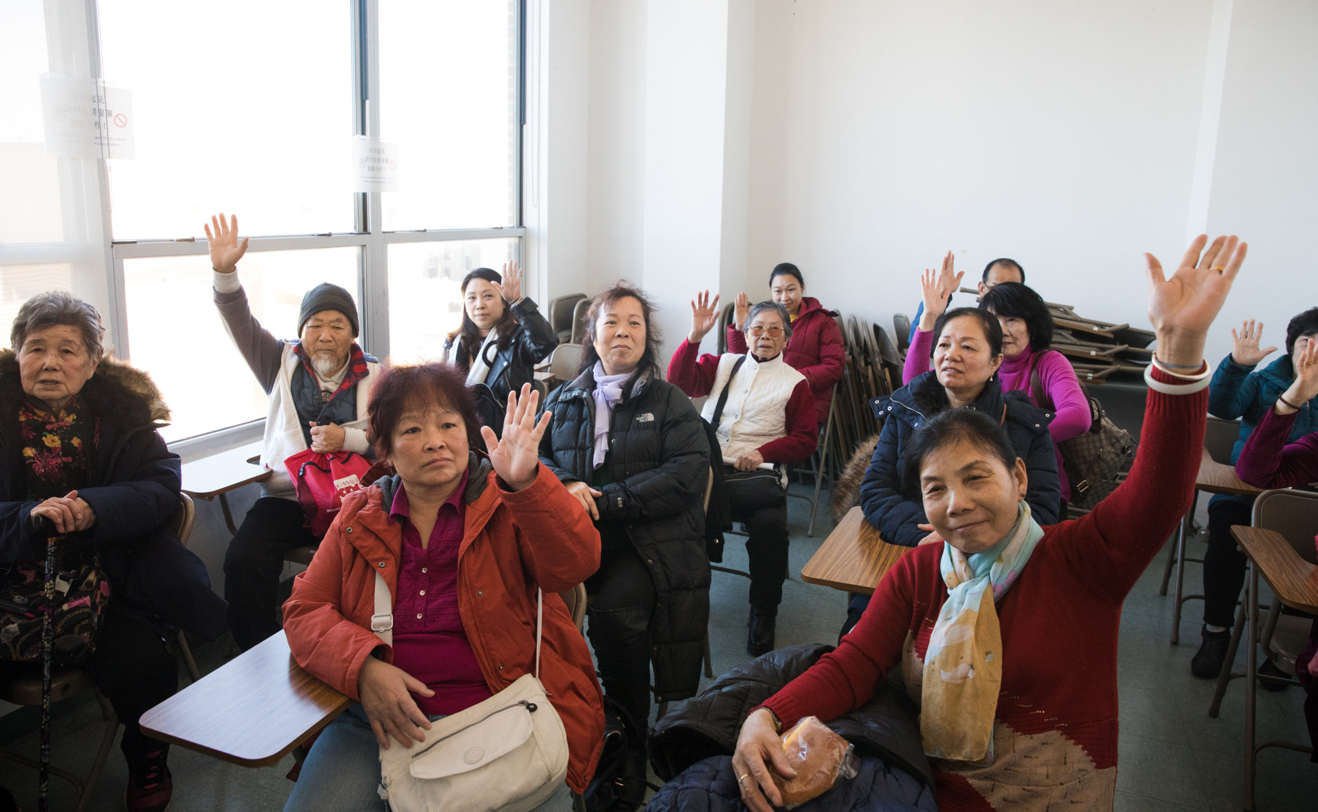 Older residents at the Chinese-American Planning Council raise their hands to affirm they've gotten their flu shots this season. Photo: Paul Frangipane/Brooklyn Eagle