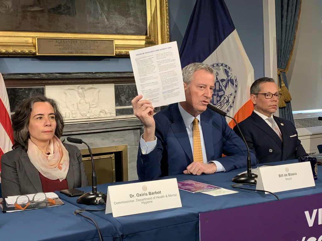 Mayor Bill de Blasio shows reporters a novel coronavirus safety tips sheet at Wednesday’s press conference. Left is NYC Health Commissioner Dr. Oxiris Barbot, and right is Dr. Raul Perea-Henze, deputy mayor for Health & Human Services. Photo: Mary Frost/Brooklyn Eagle