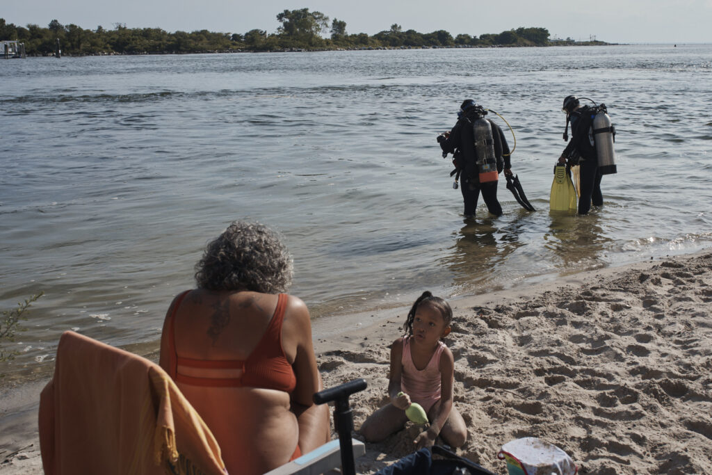 A family spends time on the beach as scuba divers, Tanasia Swift, second right, and Sarah Sears first right, prepares to enter the water during an underwater cleanup in the Queens borough of New York on Sunday, Aug. 27, 2023. A diving group takes part in a monthly cleanup at a cove in the community of Far Rockaway, about 4 miles south of John F. Kennedy Airport, to help the global effort to undo ocean pollution.Photo: Andres Kudacki/AP