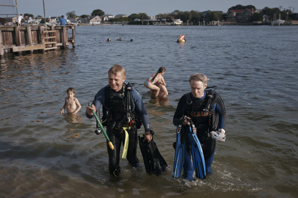 A scuba diver, center left, holds a broken broom handle found as he comes out of the water with his colleague, center right, during an underwater cleanup in the Queens borough of New York on Sunday, Aug. 27, 2023. A diving group takes part in a monthly cleanup at a cove in the community of Far Rockaway, about 4 miles south of John F. Kennedy Airport, to help the global effort to undo ocean pollution. (AP Photo/Andres Kudacki)