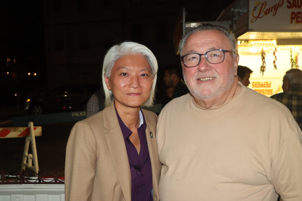 District Leaders Joseph Bova and President Irene Chu stand in front of a sausage-and-peppers stand on 15th Avenue during a Stars and Stripes Democratic Club fundraiser on Oct. 11.