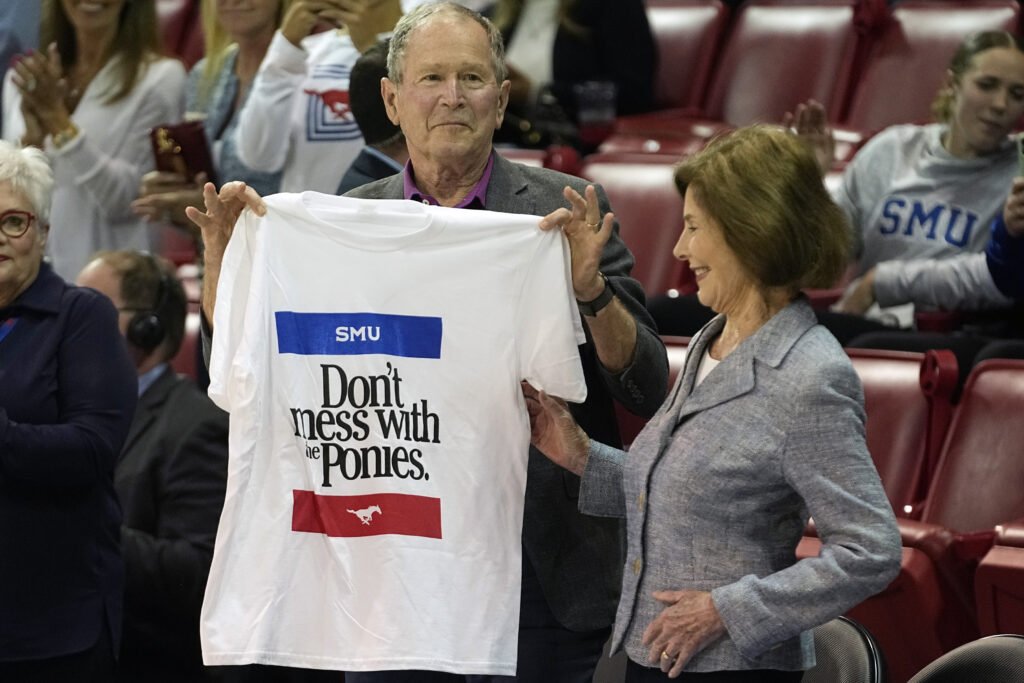 DALLAS — All strong Texas affiliations somehow boil down to horses: Former United States President George W. Bush, left, holds up a shirt with First Lady Laura Bush during an NCAA college basketball game between SMU and Texas A&M in Dallas, Tuesday, Nov. 14, 2023.Photo: LM Otero/AP