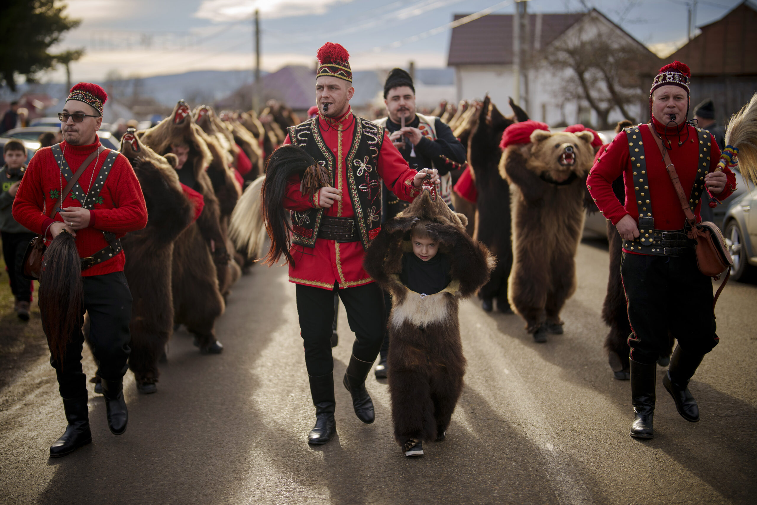 ROMANIA — Remnants of sacrificed bears, for ritual parades and dances: Members of the Sipoteni bear pack, wearing bear fur costumes, walk on a road before performing their dance for villagers in Racova, northern Romania, Tuesday, Dec. 26, 2023. The dancing bears tradition originates from the pre-Christian era, when dancers wearing colored costumes or animal furs toured from house to house in villages, singing and dancing to ward off evil.Photo: Vadim Ghirda/AP
