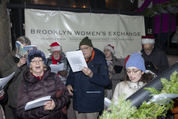 <b>MONTAGUE ST. — A 20th-century tradition celebrates with a 19th-century landmark:</b> The Montague Street holiday tree lighting ceremony, which celebrated its 71st year, recently brought into their celebration the historic Brooklyn Women’s Exchange, founded in 1854. Seen here, Grace Church choral members who sing at the tree-lighting, continued their caroling farther up Montague St. at the headquarters of the Women’s Exchange.<br>Photo: John McCarten/Brooklyn Eagle