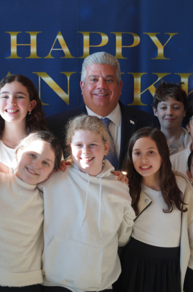 District Attorney Eric Gonzalez enjoys a cheerful moment with middle school students from Ramaz Middle School, who contributed to the Hanukkah event's festive atmosphere with their holiday songs.