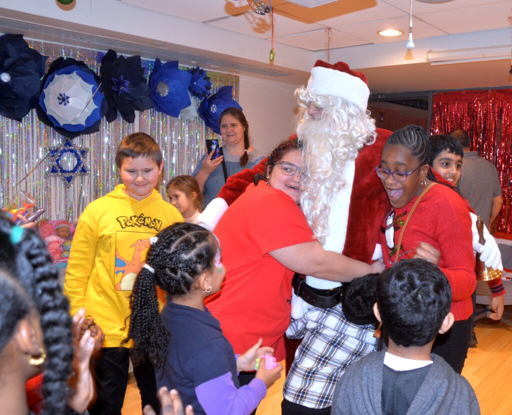Happiness and hugs for Kris Kringle at Maimonides holiday party.