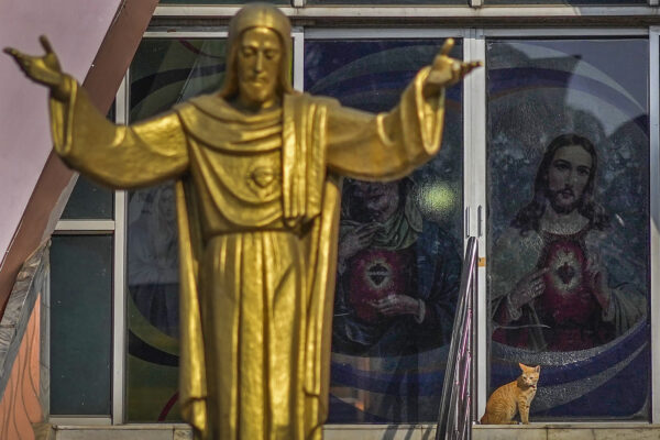 <b>INDIA — Feline Christmas curiosity does not interfere with services:</b> A cat rests on the steps of a church next to a statue of Jesus Christ as devotees pray inside on Christmas in Guwahati, India, Monday, Dec. 25, 2023.<br>Photo: Anupam Nath/AP