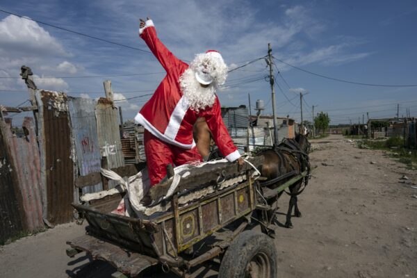 <b>BUENOS AIRES — Red suit and white beard become universal harbingers of Christmas cheer:</b> Tito Perez, dressed as Santa Claus, waves to children while standing on the back of a horse cart, at a pre-Christmas celebration organized by "Los Chicos de la Via" soup kitchen, in Buenos Aires, Argentina, Saturday, Dec. 23, 2023.<br>Photo: Rodrigo Abd/AP