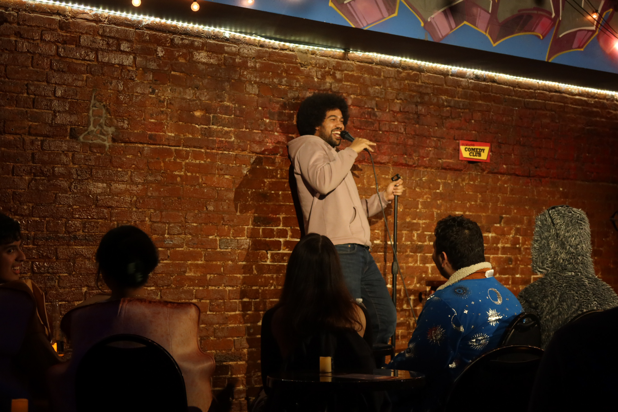 Che Durena leans on the wall on stage at St. Marks Comedy Club in NYC on Oct. 31, 2023.