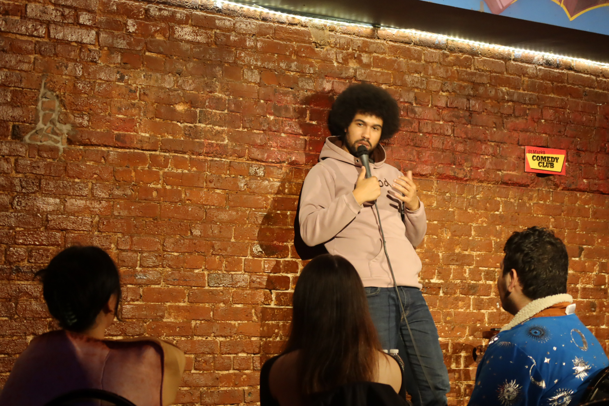 Che Durena leans on the wall on stage at St. Marks Comedy Club in NYC on Oct. 31, 2023. 