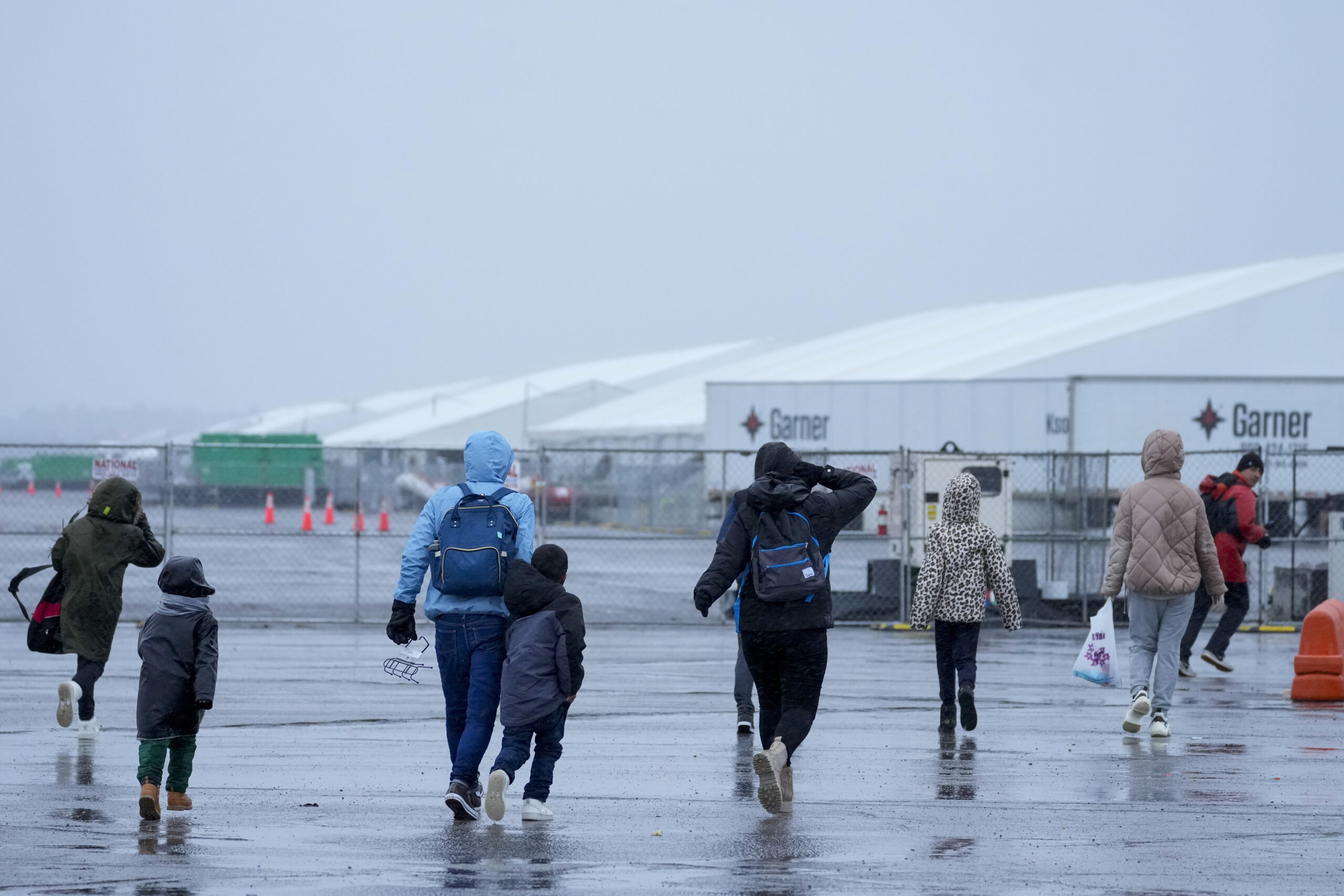 Immigrants run in the rain towards the tents at migrant housing location at Floyd Bennett Field