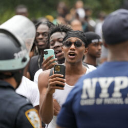 People video New York City Police Department officers as they chant anti-NYPD slogans