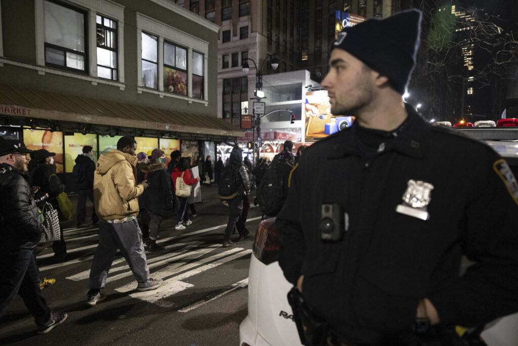A police officer watches demonstrators march during a protest, Jan. 28, 2023, in New York