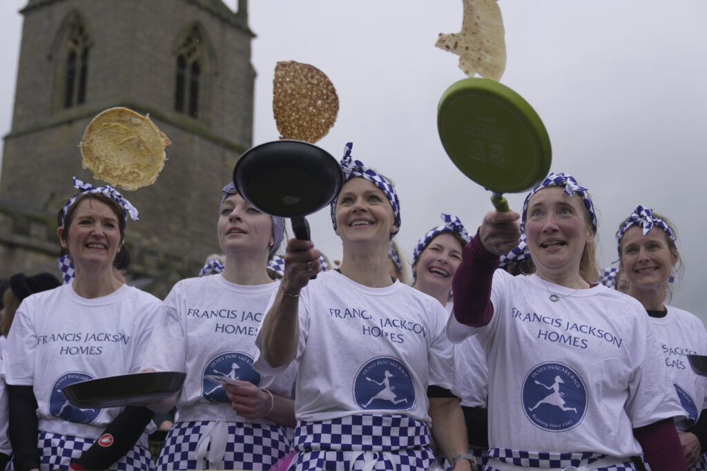 BUCKINGHAMSHIRE — The Great British Pancake-off: Pancake race winner Kaisa Larkas, center, and second place finisher Eloise Kramer, second left, and third place finisher Rebecca Budd, second right, celebrate after the annual Shrove Tuesday trans-Atlantic pancake race in the town of Olney, in Buckinghamshire, England, Tuesday, Feb. 13, 2024. Every year, women clad in aprons and head scarves from Olney and the city of Liberal, in Kansas, USA, run their respective legs of the race with pancakes in their pans. According to legend, the Olney race started in 1445 when a harried housewife arrived at church on Shrove Tuesday still clutching her frying pan with a pancake in it.Photo: Kin Cheung/AP