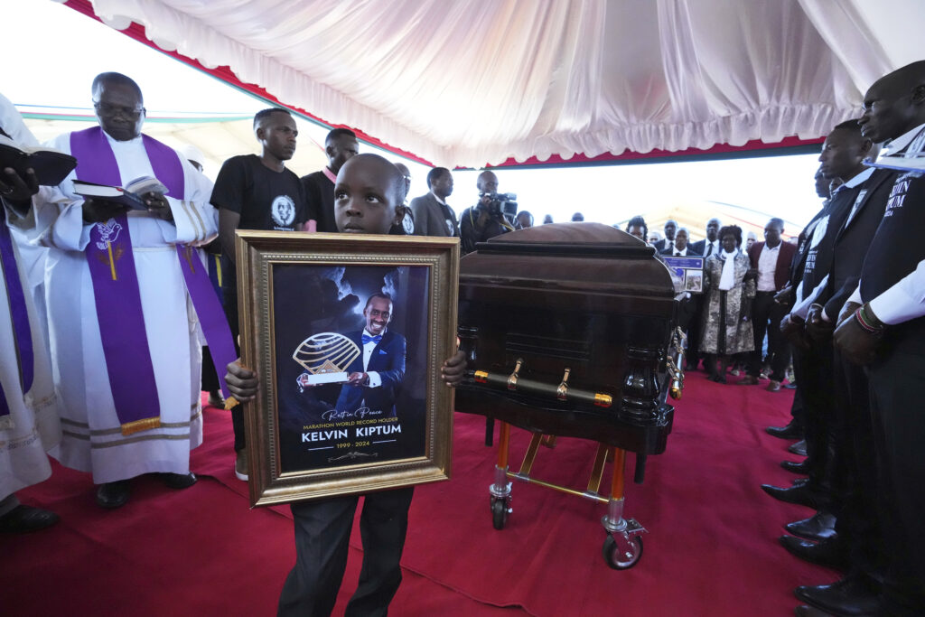 KENYA — Son of noted athlete honors his father: Caleb Kigen, the son of marathon record holder Kelvin Kiptum, holds his late father's portrait ahead of his burial in Elgeyo Marakwet, Kenya, Friday. Feb. 23, 2024. World marathon record holder Kelvin Kiptum was buried Friday following his death in a road accident, as Kenyans castigated the government for not doing enough to protect and support the country's famed athletes.Photo: Brian Inganga/AP