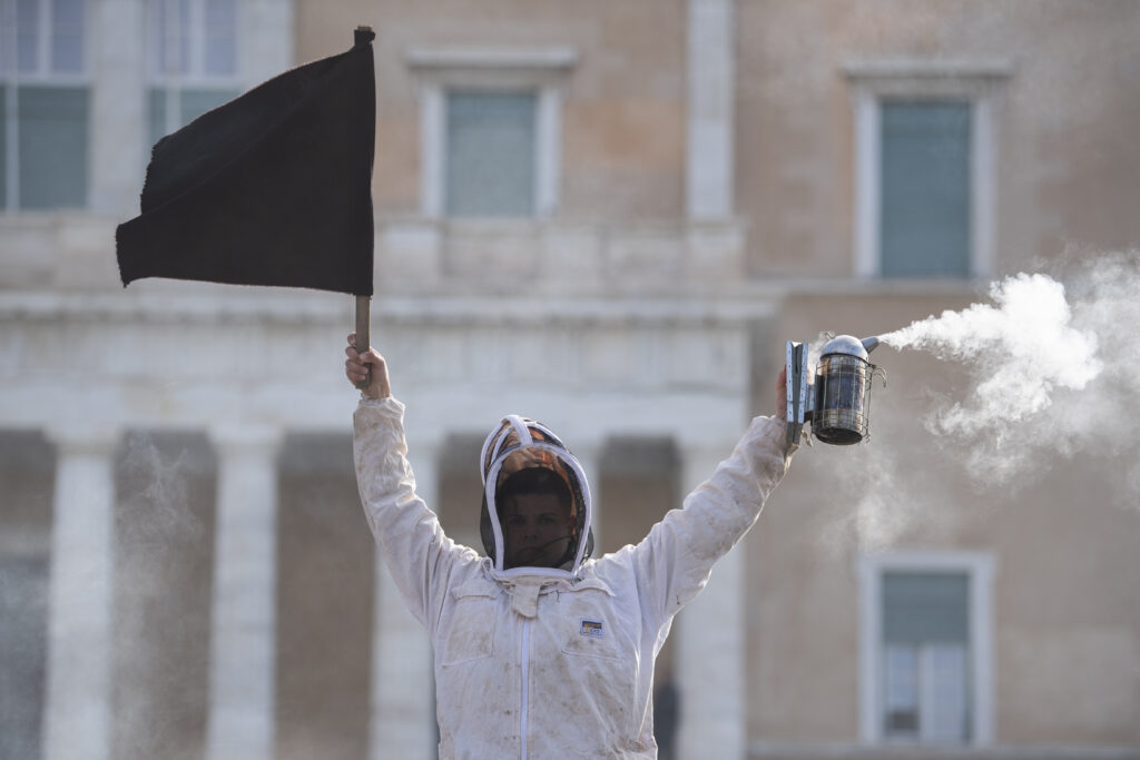 ATHENS — Beekeepers abuzz with a stinging issue: A beekeeper holds a black flag in front of the Greek Parliament during a demonstration in central Athens, Greece, Thursday, Feb. 22, 2024. Beekeepers from around the country rallied in Syntagma Square with demands, including the end of naming imported honey “Greek.”Photo: Michael Varaklas/AP