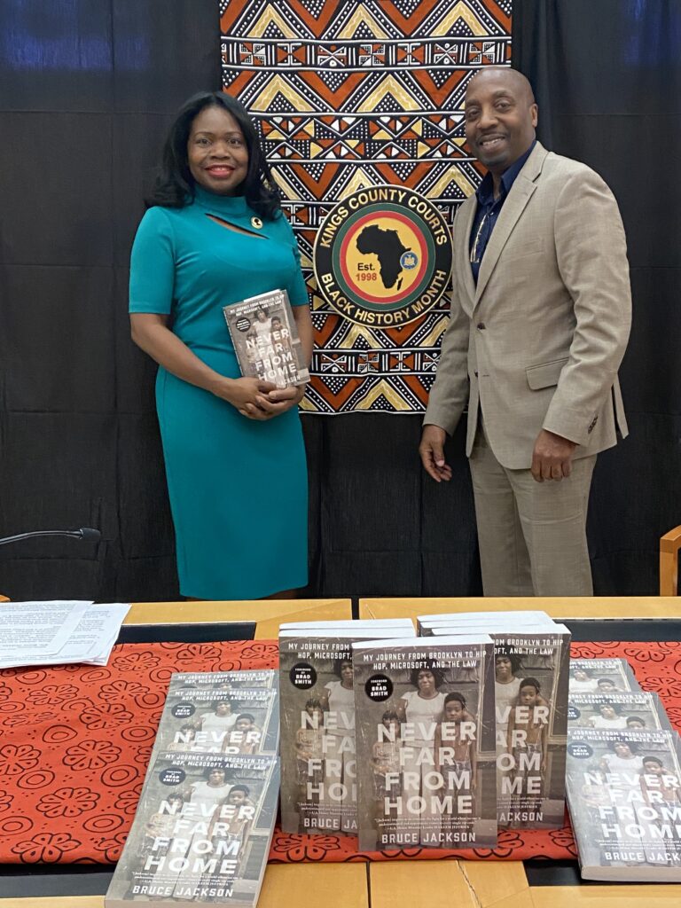 Hon. Genine Edwards, the event's engaging moderator, shares a moment with Bruce Jackson, proudly displaying his memoir 'Never Far From Home', a testament to resilience and success.Photo courtesy of Hon. Genine Edwards