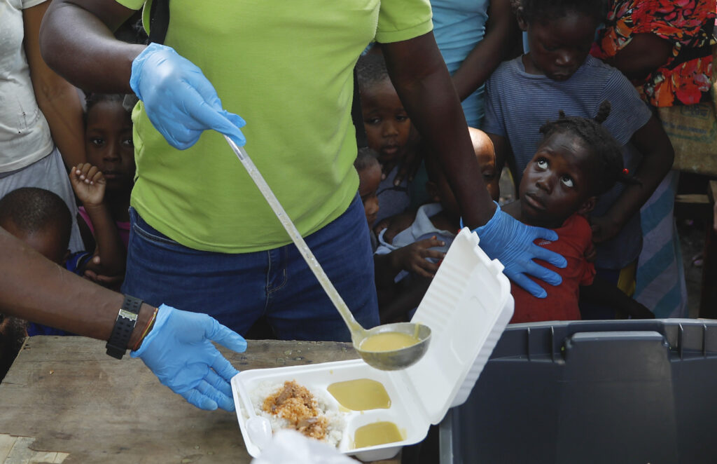 PORT-AU-PRINCE — Mitigating the impact of gang violence: A server ladles soup into a container as children line up to receive food at a shelter for families displaced by gang violence, in Port-au-Prince, Haiti, Thursday, March 14, 2024.Photo: Odelyn Joseph/AP