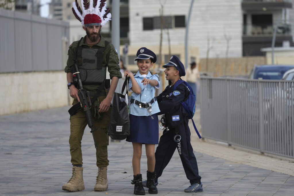 ISRAEL — While police wear a head-dress for Purim, kids dress up as cops: Israeli children wear police costumes as they stand with an Israeli soldier as they celebrate the Jewish holiday of Purim, in Sderot, southern Israel, more than five months after a cross-border attack by Hamas, Friday, March 22, 2024. According to the Jerusalem Post, Israeli army costumes have become the most popular choice for Purim this year. The Jewish holiday of Purim commemorates the Jews’ salvation from genocide in ancient Persia, as recounted in the Book of Esther.Photo: Tsafrir Abayov/AP