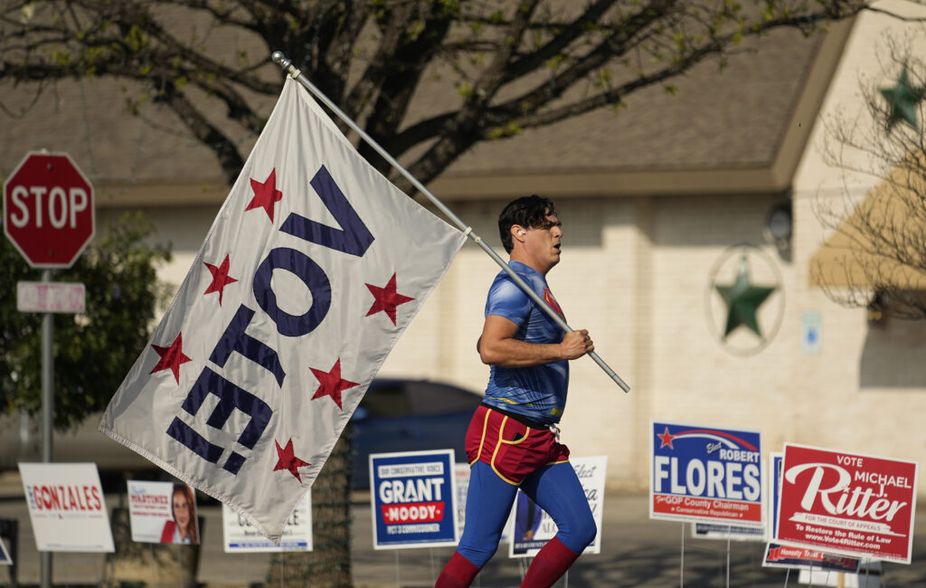 SAN ANTONIO — Voting — the common person's superpower: Dressed as Superman and holding a "Vote!" flag, Artist David Alcantar jogs past a polling site, Tuesday, March 5, 2024, in San Antonio. The flag and costume are part of an art project to encourage voting.Photo: Eric Gay/AP