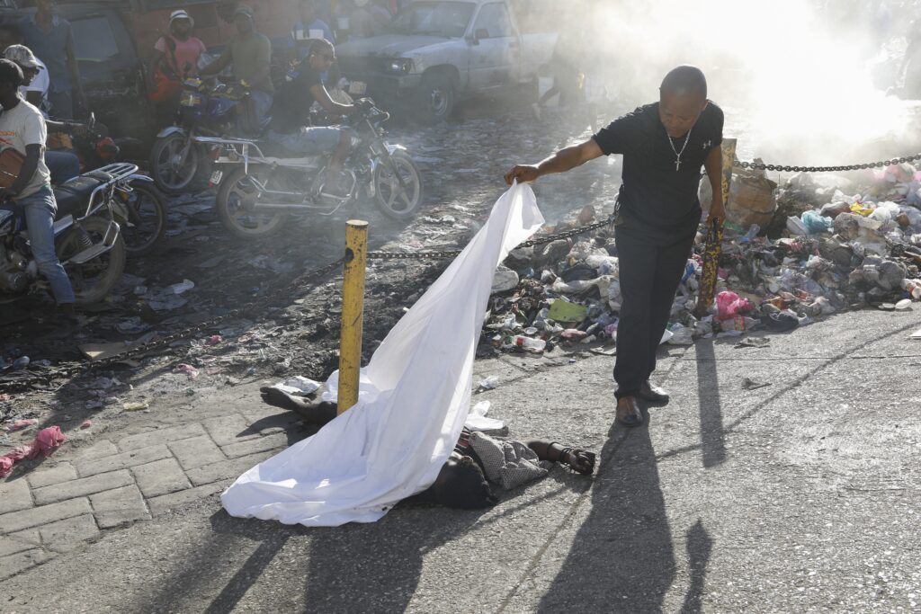 PORT-AU-PRINCE — Grim morning greeting in the world of governance by gangs: A person lifts a sheet to look at the identity of a body lying on the ground after an overnight shooting in the Petion Ville neighborhood of Port-au-Prince, Haiti, Monday, March 18, 2024.Photo: Odelyn Joseph/AP
