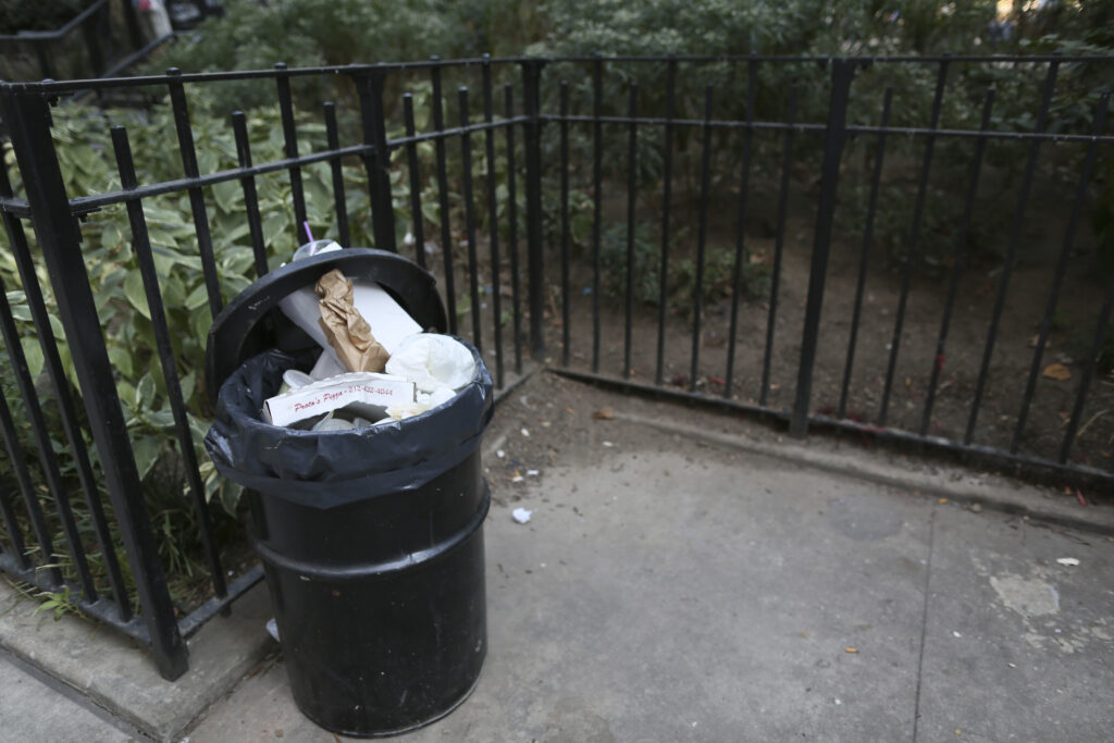 An open and overflowing garbage container is seen next to a park in the Chinatown neighborhood of New York.