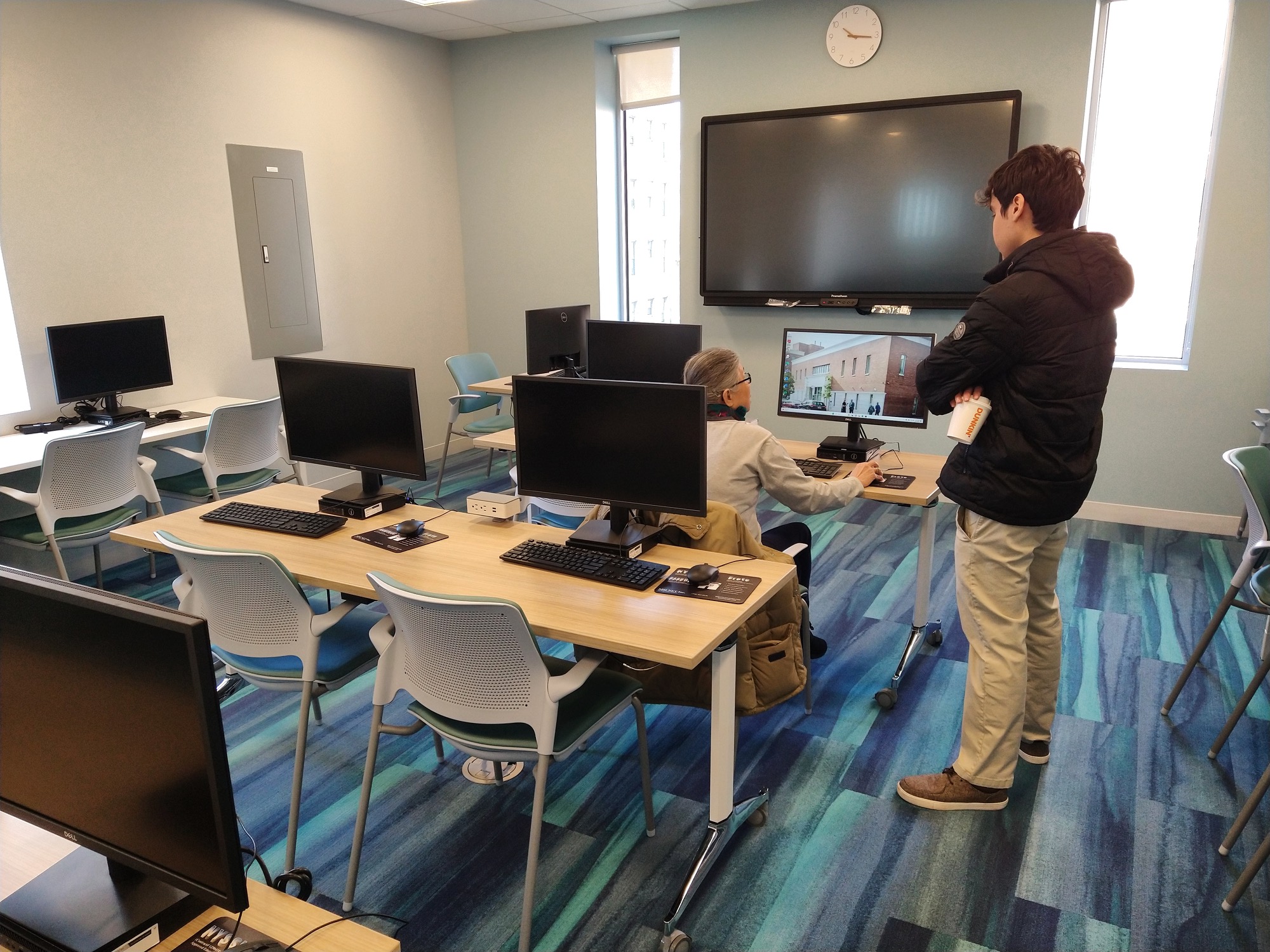 A staff member assisting an older adult in the computer lab at Bay Ridge Center Opening.