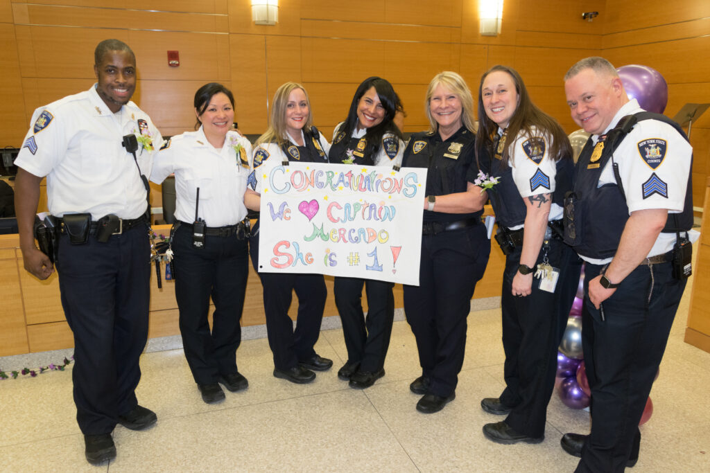 Sgt. Shaqwan Gardner, Sgt. Mary Mido Wu, Sgt. Jeannine Ruiz, Capt. Erica Mercado, C.O. Diane Ambery, Sgt. Stacey Walder and Sgt. Vincent Morena, standing together with a sign they made for Capt. Mercado at SJDEJC Women's History Month.