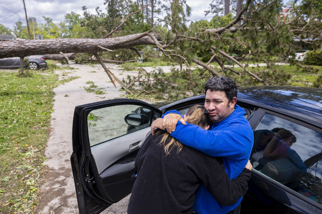 Max Gonzales hugs his girlfriend, April Martin, while leaning against their car taking in the surrounding tornado damage where his parents, Michael and Lilian Bray, live in Slidell, La., on Thursday, April 11, 2024. The neighborhood was picking up the pieces the day after a tornado swept through the area. (Chris Granger/The Times-Picayune/The New Orleans Advocate via AP)