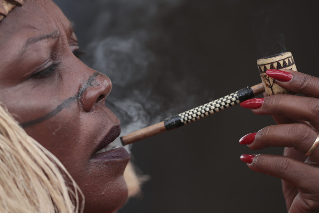 An Indigenous woman smokes a pipe during the 20th annual Free Land Indigenous Camp in Brasilia, Brazil, Tuesday, April 23, 2024. The 7-day event aims to show the unity of Brazil's Indigenous peoples in their fight for the demarcation of their lands and their rights. (AP Photo/Luis Nova)