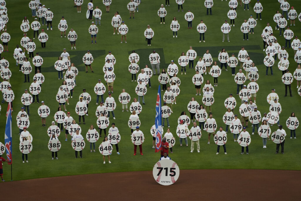 In honor of the 50th anniversary of Hank Aaron breaking Babe Ruth's home run record 715 fans match onto the field to each holding a sign to commemorate an Aaron home run before a baseball game between New York Mets and Atlanta Braves Monday, April 8, 2024, in Atlanta. Aaron passed Ruth on April 8, 1974. (AP Photo/John Bazemore)