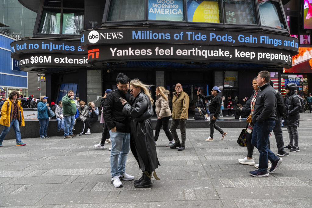 People walk around Times Square as news tickers display news about the earthquake on Friday, April 5, 2024, in New York.