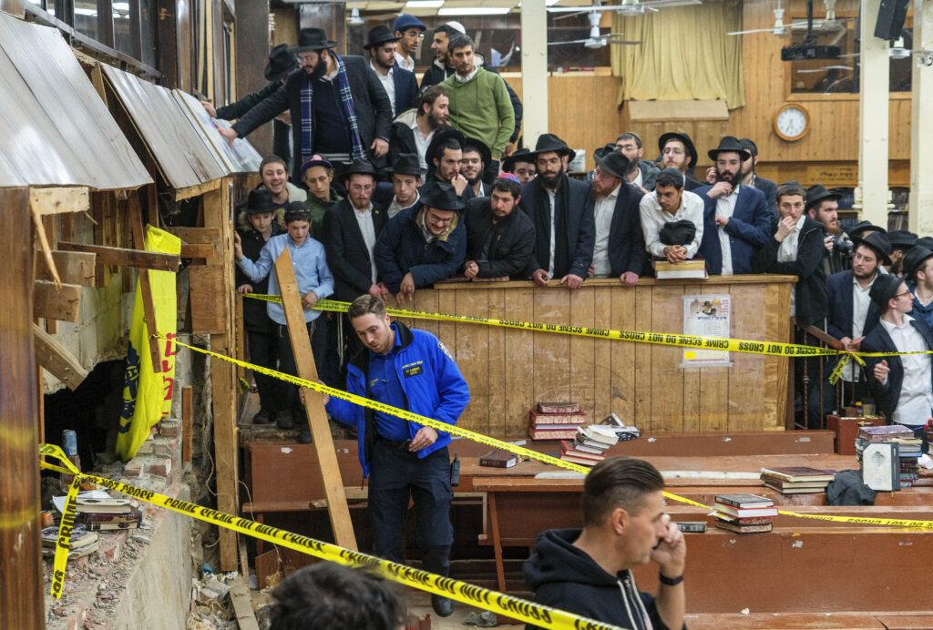 Hasidic Jewish students observe as law enforcement establishes a perimeter around a breached wall in the synagogue that led to a tunnel dug by students, Jan. 8, 2024, in New York.