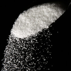 Granulated sugar is poured using a spoon.