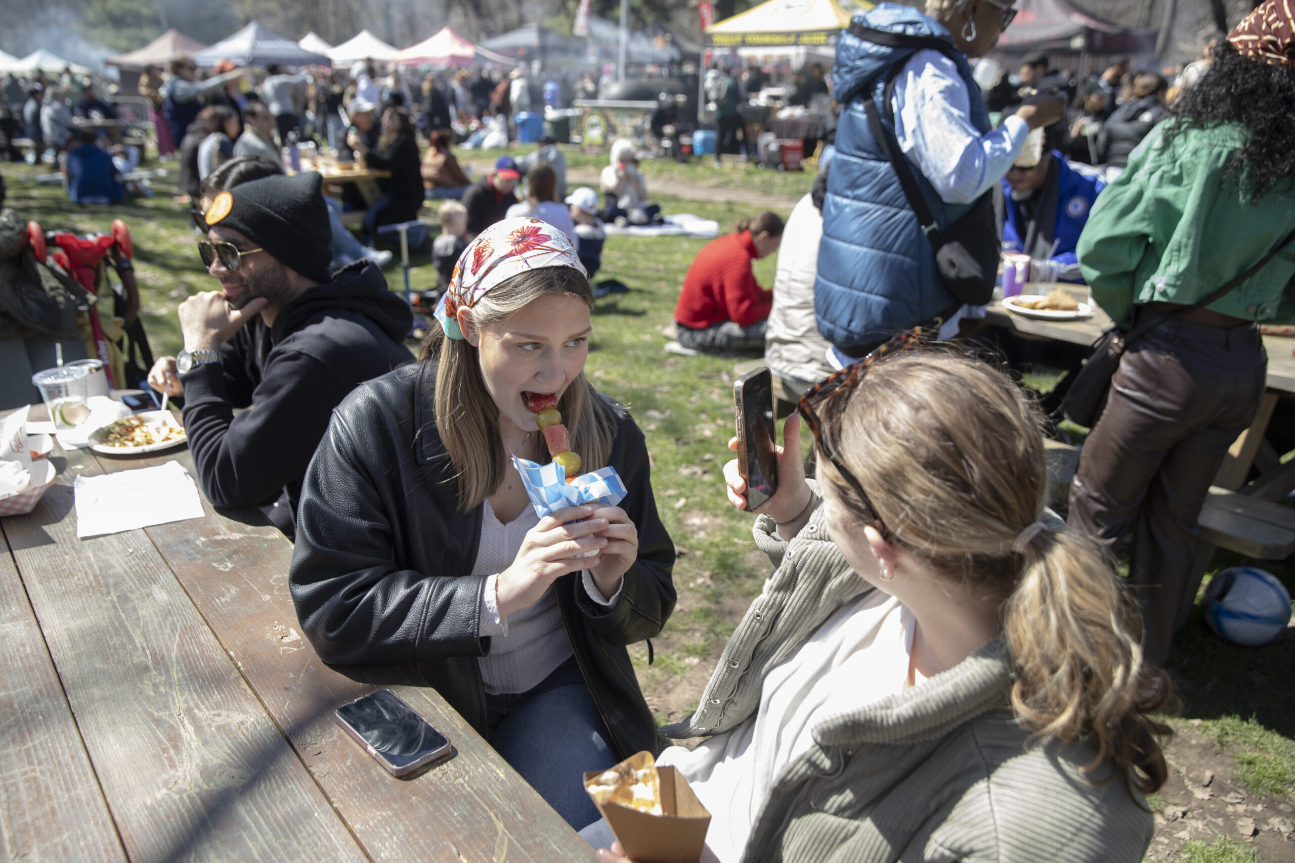 Maddie Musgraves takes a video of Riley Savage eating a piece of candied fruit at Prospect Park Smorgasburg.