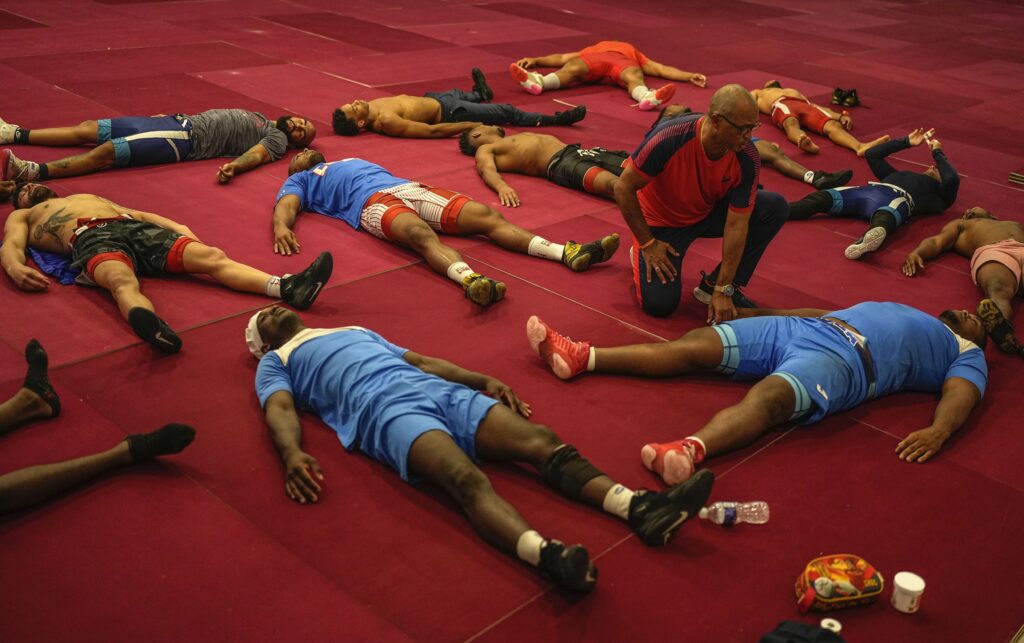 Members of the Cuban national Greco-Roman wrestler team stretch out on the mat during a training session in Varadero, Cuba, Wednesday, April 3, 2024. Teammate Mijain Lopez Nunez is part of the Cuban delegation headed to Paris in pursuit of a fifth Olympic gold to mark the end of his career. (AP Photo/Ramon Espinosa)