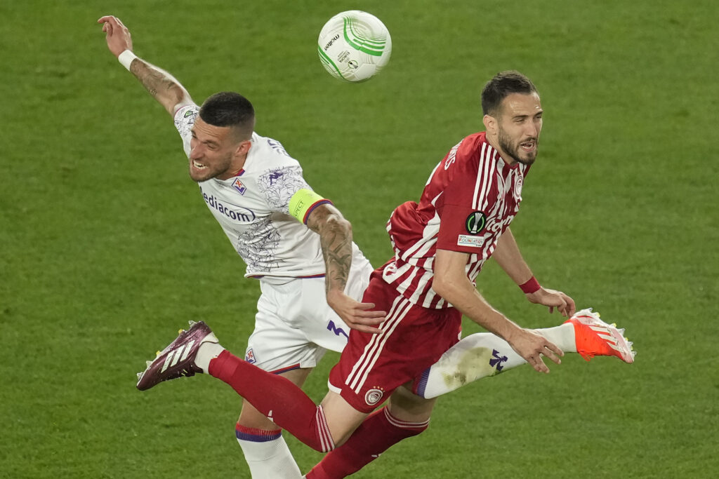 Olympiacos' Kostas Fortounis jumps for a header with Fiorentina's Cristiano Biraghi during the Conference League final soccer match between Olympiacos FC and ACF Fiorentina at OPAP Arena in Athens, Greece, Wednesday, May 29, 2024. (AP Photo/Petros Karadjias)