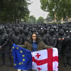 A woman holds a Georgian national and an EU flags in front of riot police blocking a street to prevent demonstrators during an opposition protest against "the Russian law" near the Parliament building in the center of Tbilisi, Georgia, Tuesday, May 14, 2024. The Georgian parliament on Tuesday approved in the third and final reading a divisive bill that sparked weeks of mass protests, with critics seeing it as a threat to democratic freedoms and the country's aspirations to join the European Union. (AP Photo/Zurab Tsertsvadze)