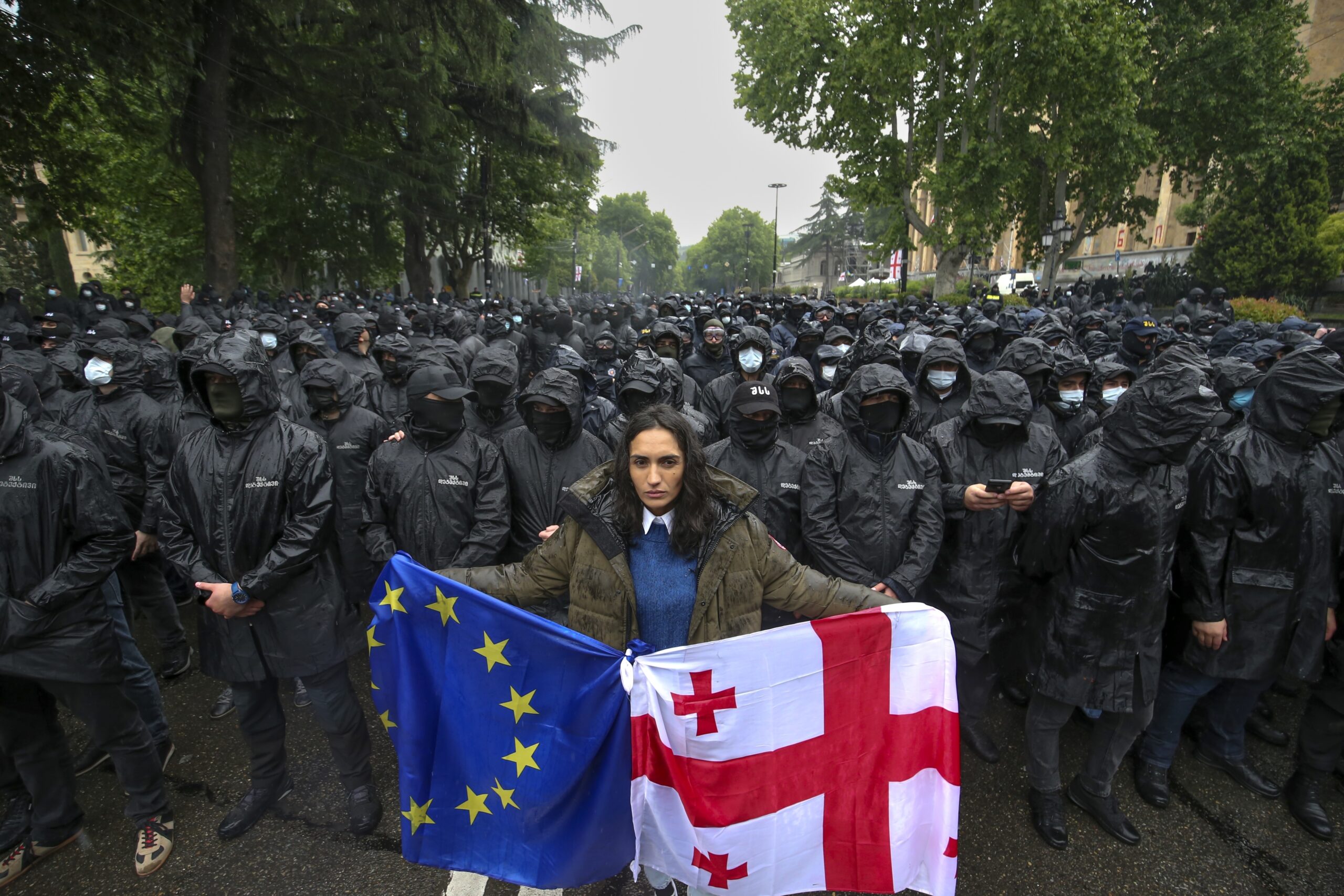A woman holds a Georgian national and an EU flags in front of riot police blocking a street to prevent demonstrators during an opposition protest against "the Russian law" near the Parliament building in the center of Tbilisi, Georgia, Tuesday, May 14, 2024. The Georgian parliament on Tuesday approved in the third and final reading a divisive bill that sparked weeks of mass protests, with critics seeing it as a threat to democratic freedoms and the country's aspirations to join the European Union. (AP Photo/Zurab Tsertsvadze)