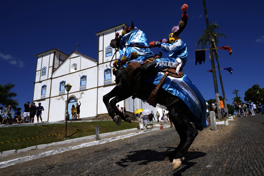 A horseman, wearing a decorative bull mask, and mounted on a prancing horse, attends the Feast of the Divine celebrations, backdropped by the Our Lady of the Rosary Parish, as part of the “Cavalhadas” festival, in Pirenopolis, Goias state, Brazil, Saturday, May 18, 2024. The tradition of the "Cavalhadas" or masked horsemen's festival was brought to Brazil in the 1800s by a Portuguese priest to celebrate the "Holy Spirit" and to commemorate the medieval victory of Iberian Christian knights over the Moors. (AP Photo/Eraldo Peres)