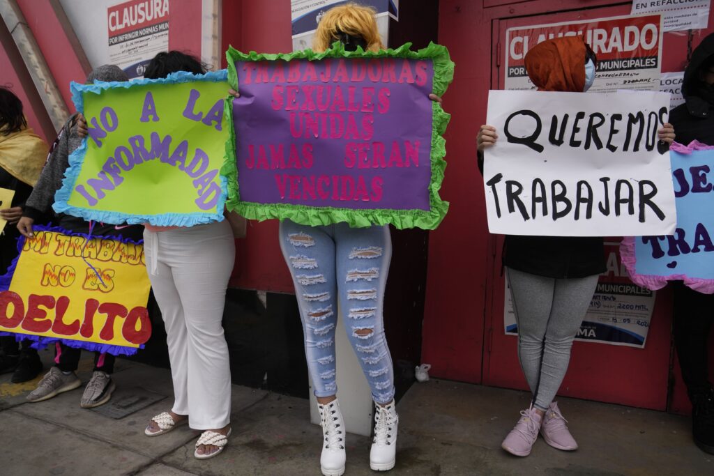 Masked sex workers protest outside their brothel "Las Cucardas" after it was shuttered by city authorities in Lima, Peru, Monday, May 20, 2024. The municipal government closed the brothel on May 15 for not having their building up to code. The signs read in Spanish, from left, "No to informality," "United sex workers will never be defeated," and "We want to work." (AP Photo/Martin Mejia)