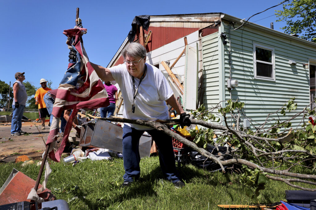 Patti Manley, 69, moves a shredded American flag as she gathers branches from the backyard of her mother's home on Morningdale Place in Mehlville, Mo. on Monday, May 27, 2024, following a violent storm and possible tornado Sunday evening. Manley was staying with her mother Jackie Moloney, 88, when the storm hit. She and her mother rode it out in an interior bathroom. (Robert Cohen/St. Louis Post-Dispatch via AP)