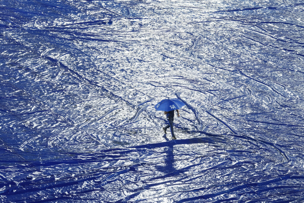A ground staff walks with an umbrella during rain before the start of the Indian Premier League cricket match between Gujrat Titans and Sunrisers Hyderabad in Hyderabad, India, Thursday, May 16, 2024. (AP Photo /Mahesh Kumar A.)