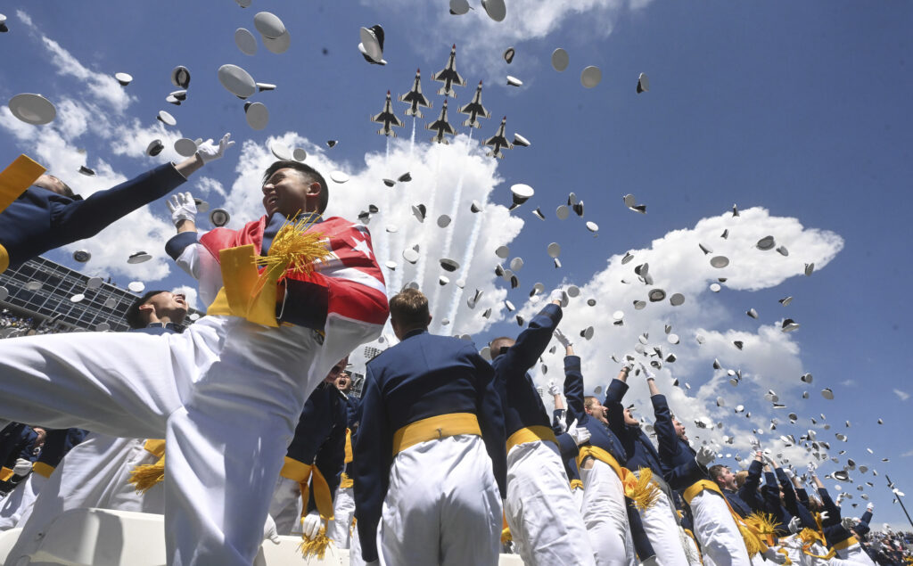 Cadet Jonathan Loh, left, from Singapore, and the class of 2024 at the United States Air Force Academy toss their hats in the air as the Thunderbirds fly over Falcon Stadium, Thursday, May 30, 2024, at the conclusion of the commencement ceremony in Colorado Springs, Colo. (Jerilee Bennett/The Gazette via AP)