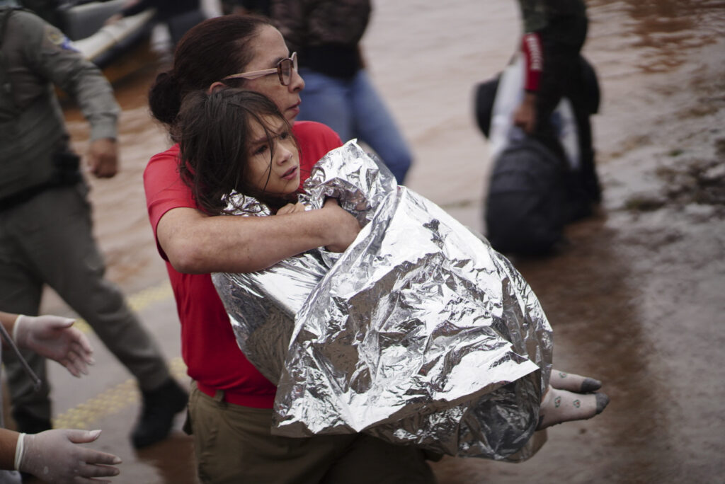 A firefighter carries a girl rescued from an area flooded by heavy rains in Porto Alegre, Rio Grande do Sul state, Brazil, Saturday, May 4, 2024. (AP Photo/Carlos Macedo)