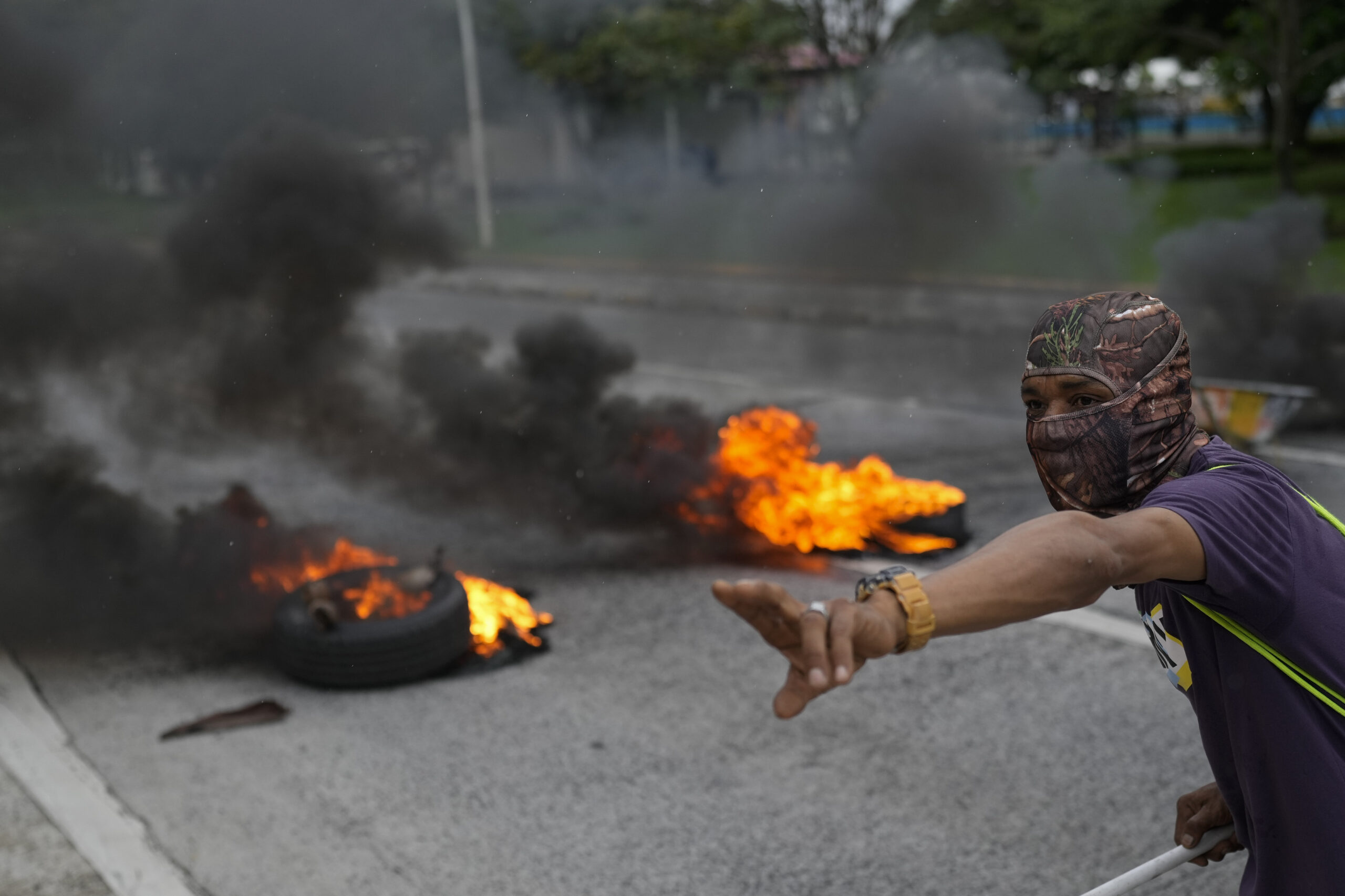 A masked protester shouts to his colleagues as they block a street with burning tires as part of the national strike by the construction union, SUNTRACS, in Panama City, Thursday, June 20, 2024. (AP Photo/Matias Delacroix)