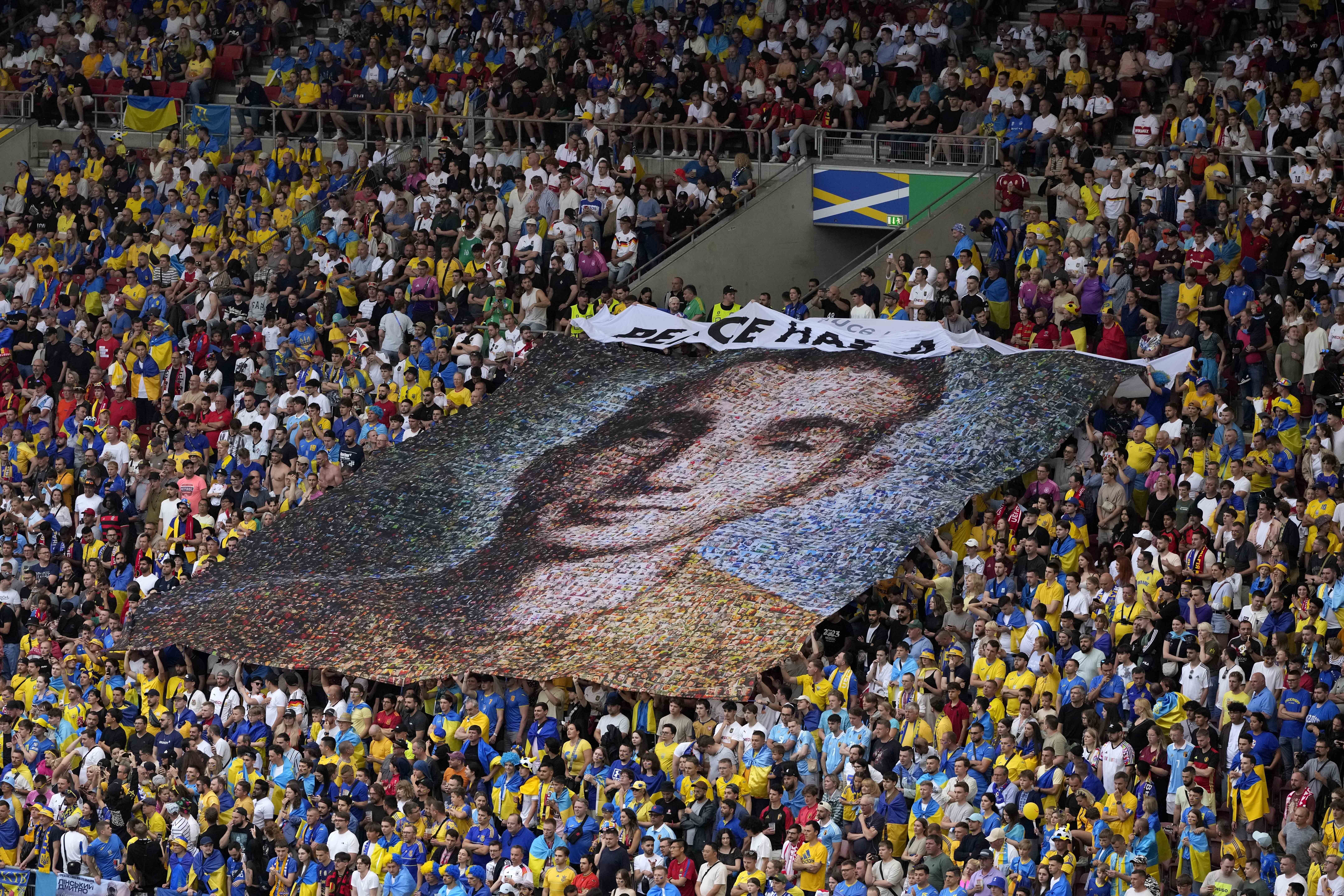 Ukraine fans display a banner reading 'Peace has a price' and a portrait of Nazariy Hryntsevich a fallen soldier a football fan, during a Group E match between Ukraine and Belgium at the Euro 2024 soccer tournament in Stuttgart, Germany, Wednesday, June 26, 2024. (AP Photo/Antonio Calanni)