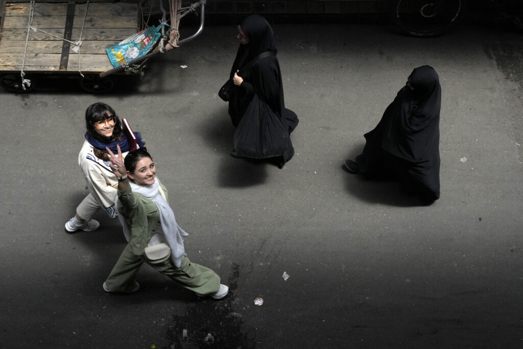 An Iranian woman without wearing her mandatory Islamic headscarf flashes a victory sign as two head-to-toe veiled women walk at the old main bazaar of Tehran, Iran, Thursday, June 13, 2024. (AP Photo/Vahid Salemi)