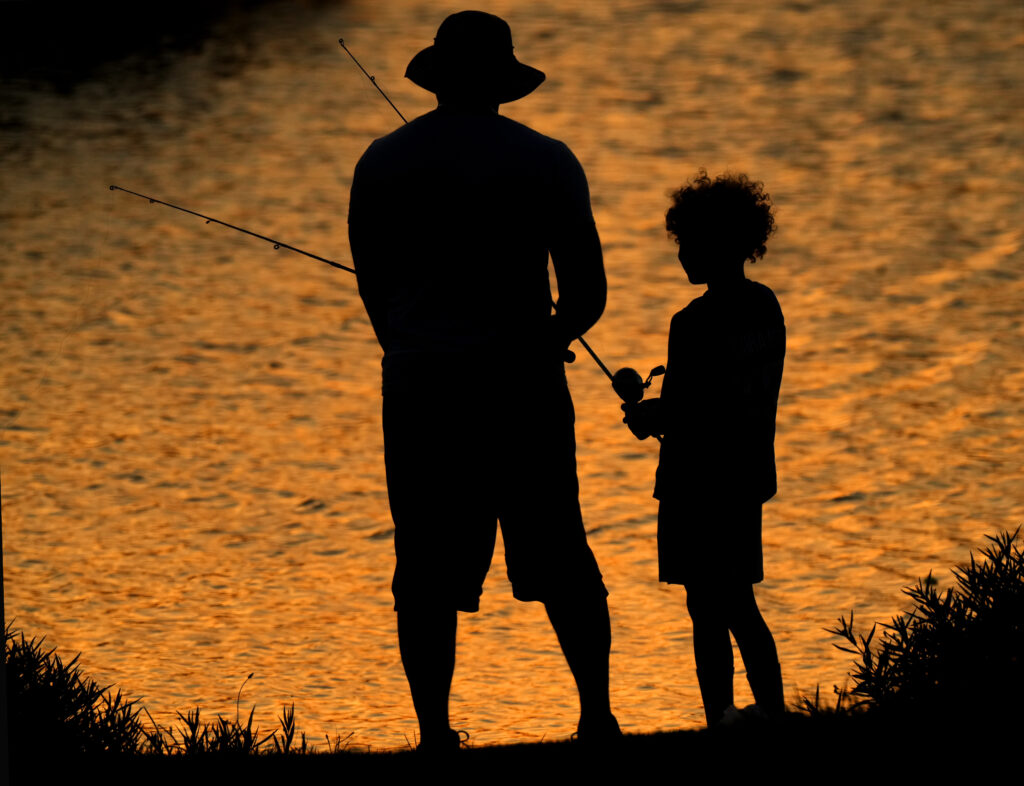 A man and a boy fish on Shawnee Mission lake at the end of a warm Monday, June 17, 2024, in Shawnee, Kan. (AP Photo/Charlie Riedel)